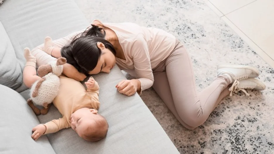 Mother resting her head on the couch near her sleeping baby